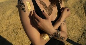 crop anonymous female with tattoos and curly hair in black top standing with hands crossed in sand a