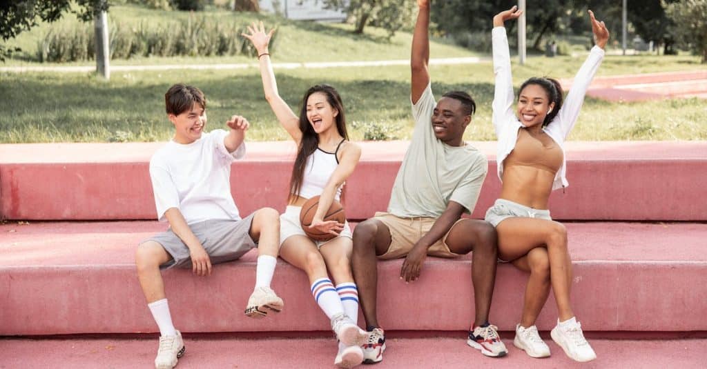 delighted-multiethnic-friends-raising-arms-happily-on-bench-in-park